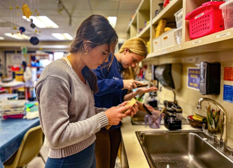 Juniors Marion Fertitta and Blakely Brown use a rough wooden brush and soap to scrub the remaining clay off their piece of silver. This is the last step in the process before the silver is use for a piece of jewelry.