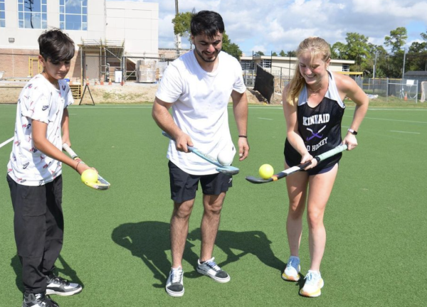 Junior and field hockey player Caroline Raynes does a warmup exercise with two refugee students.