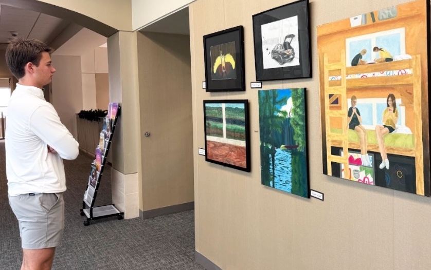 Freshman John Rosser admires junior Molly Jane Dunn's paintings about her experience with a camp she’s been attending since she was five. Rosser says, “I was drawn to her paintings because the colors in the painting really made it pop, and it caught my eye.” Dunn’s art was featured in the mediums: gouache, watercolor, oil paint, drawing pencils, and Prismacolor.