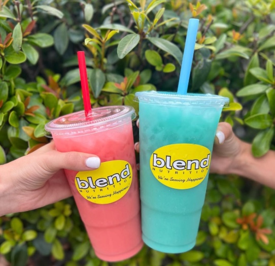 Two students hold up energy teas from Blend Nutrition.